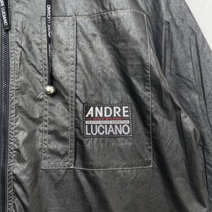 May include: A black jacket with a zip fastening and a patch on the left chest that reads "ANDRE ITALY MILANO VESTITO MOLTO SIMPATICO LUCIANO".