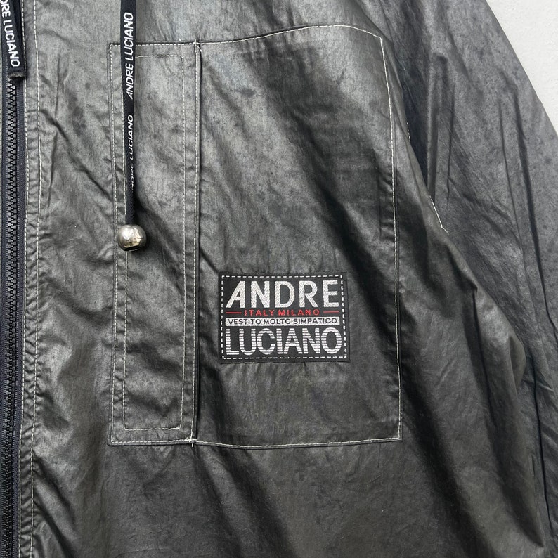 May include: A black jacket with a zip fastening and a patch on the left chest that reads "ANDRE ITALY MILANO VESTITO MOLTO SIMPATICO LUCIANO".