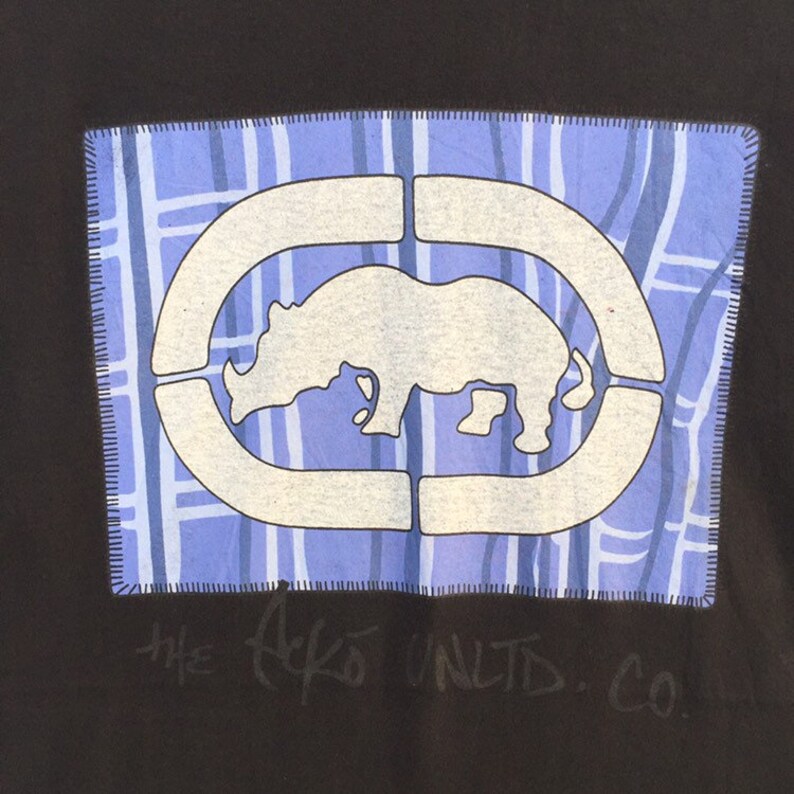 May include: Black t-shirt featuring a blue square patch with a white rhino logo inside a white outline. The patch has a blue and white grid pattern. The text "THE ECKO UNLTD. CO." is written in cursive below the patch.