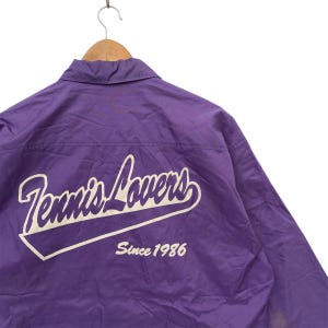 May include: Purple nylon jacket with a white "Tennis Lovers Since 1986" logo on the back.