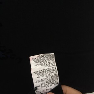 May include: A black garment with a white tag attached. The tag has text in multiple languages, including French and English, detailing care instructions such as hand wash, dry flat, and cool iron.