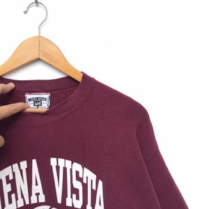 May include: Burgundy sweatshirt with white lettering that reads "Lena Vista" on the front. The sweatshirt has a Lee label with the text "Cross Grainy" on it.
