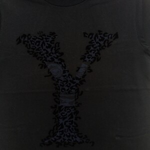 May include: Black t-shirt featuring a large, stylized letter "Y" in a dark blue leopard print design. The letter incorporates floral elements and a band detail, creating a unique graphic.