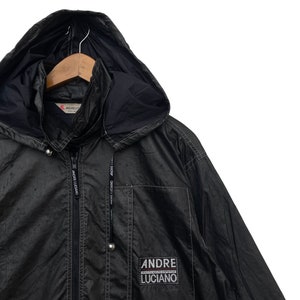 May include: A black hooded jacket with a zip fastening and a logo patch that reads "ANDRE LUCIANO" on the lower right side. The jacket has a drawstring hood and two pockets.