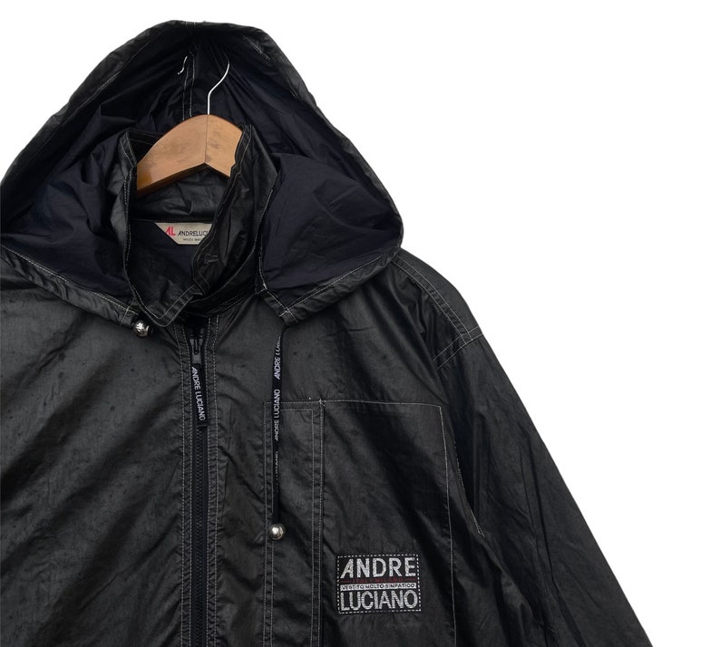 May include: A black hooded jacket with a zip fastening and a logo patch that reads "ANDRE LUCIANO" on the lower right side. The jacket has a drawstring hood and two pockets.