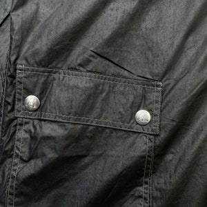 May include: A black jacket with a large pocket on the front. The pocket has two silver buttons with a logo on them.