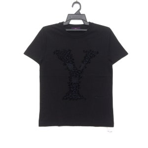 May include: Black short-sleeved t-shirt with a large, dark leopard-print letter "Y" on the front. The shirt is hanging on a black hanger against a white background. The brand name "VC" is visible on the hanger.