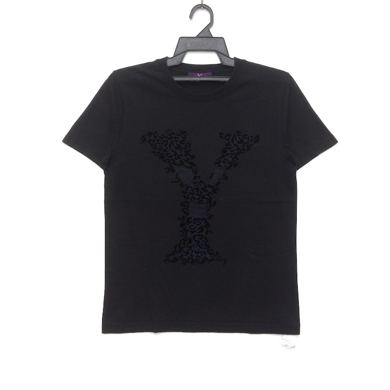 May include: Black short-sleeved t-shirt with a large, dark leopard-print letter "Y" on the front. The shirt is hanging on a black hanger against a white background. The brand name "VC" is visible on the hanger.