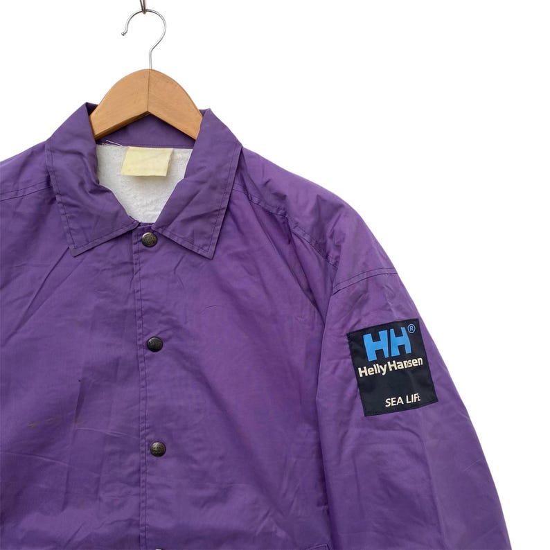 May include: A purple Helly Hansen jacket with a snap closure and a logo patch on the sleeve that reads "Helly Hansen Sea Life".