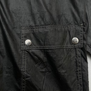 May include: Black jacket with a large pocket on the back. The pocket has two silver buttons with a logo on them.
