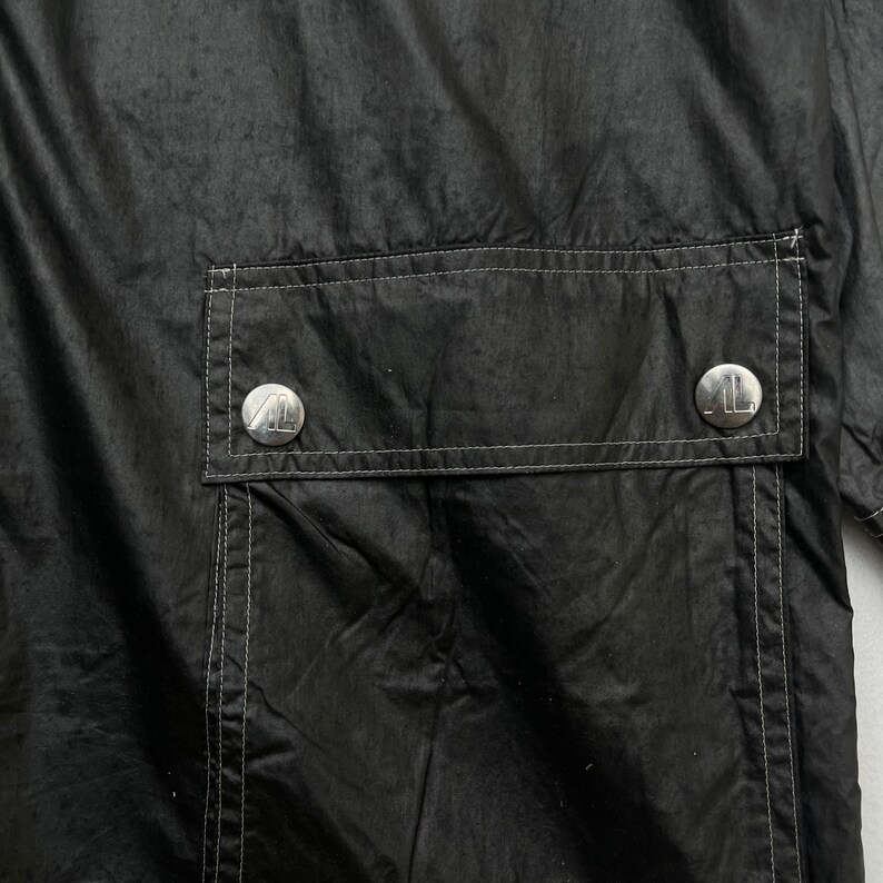 May include: Black jacket with a large pocket on the back. The pocket has two silver buttons with a logo on them.