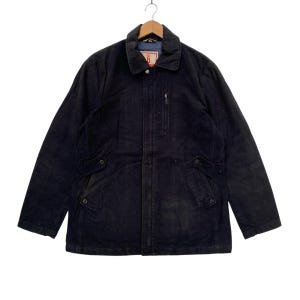 May include: A dark blue corduroy jacket with a zipper closure and two flap pockets on the front. The jacket has a stand-up collar and a button closure at the neck.