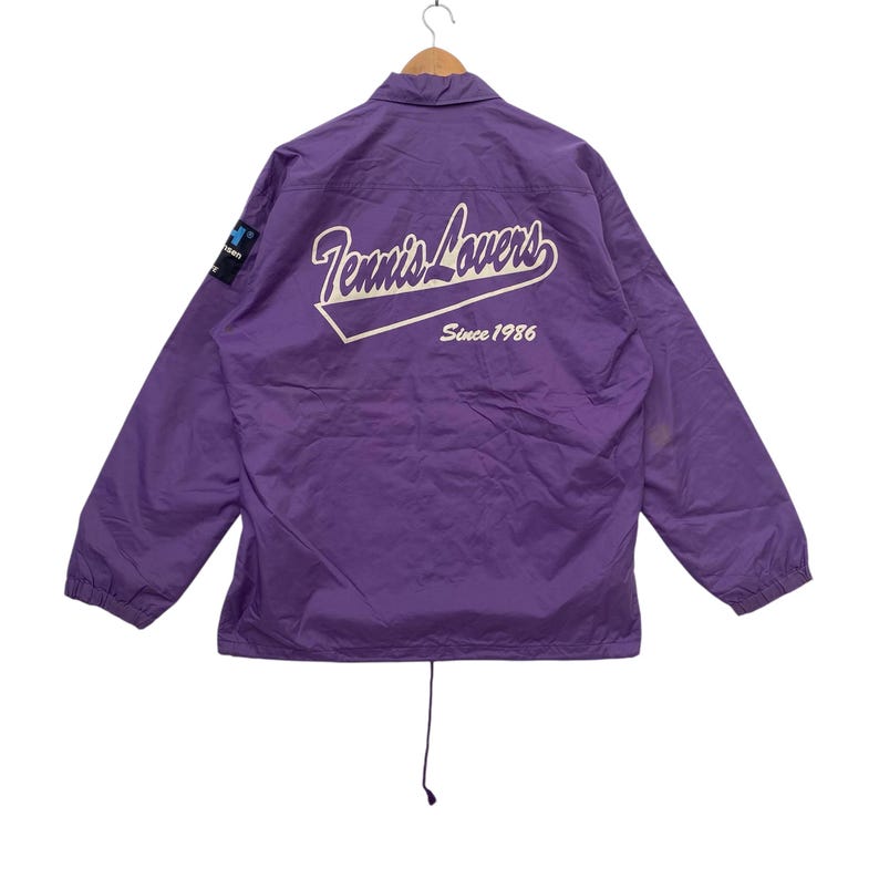 May include: Purple nylon jacket with a white logo that says "Tennis Lovers Since 1986".