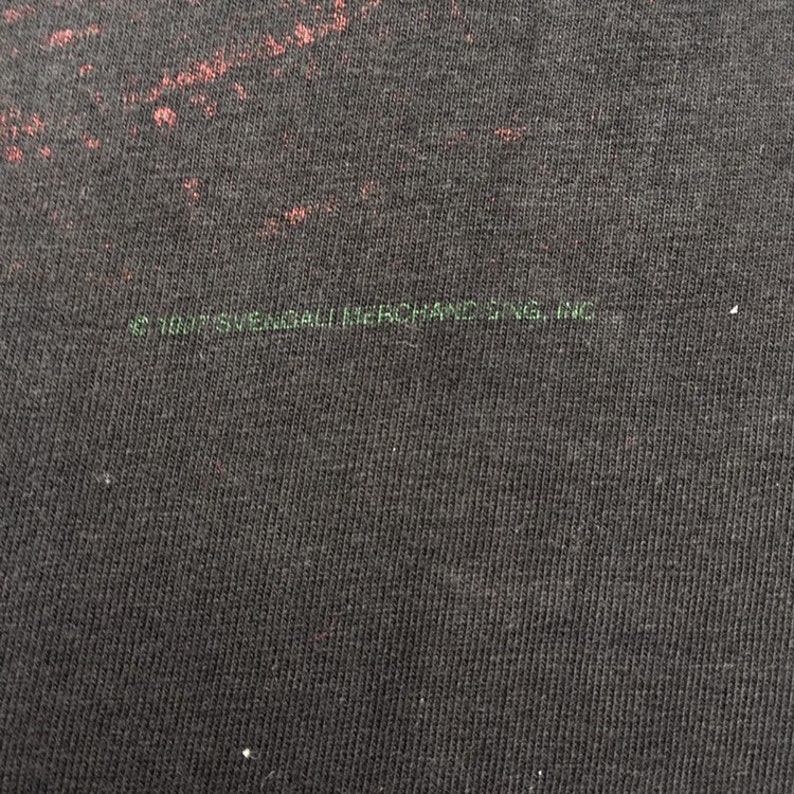 May include: Close-up of a black t-shirt with a faded green print that reads "1997 Sweatband Merch. Inc."