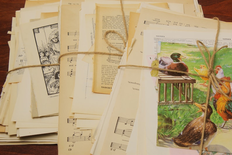 May include: A stack of vintage paper ephemera, including sheet music, book pages, and illustrations, tied together with twine. The paper is cream-coloured and has a distressed, aged look.