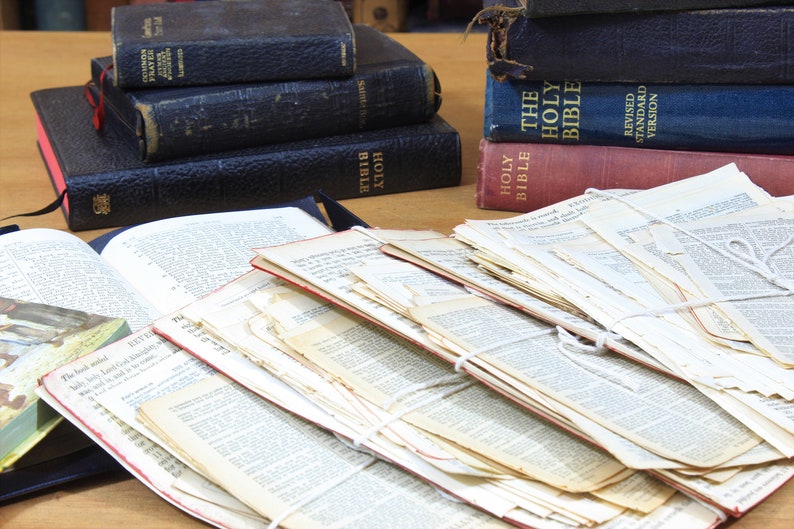 Może przedstawiać: Stos starych, zużytych i bardzo cenionych Biblii, z kartkami związanymi sznurkiem. Biblie są w r&oacute;żnych odcieniach niebieskiego i czerwonego z złotymi napisami. Tekst na okładce g&oacute;rnej Biblii brzmi "The Holy Bible, Revised Standard Version".