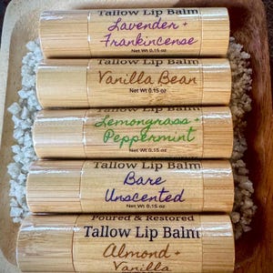 Könnte beinhalten: Fünf Bambus-Lippenbalsam-Tuben mit handgeschriebenen Etiketten. Zu den Geschmacksrichtungen gehören Lavendel + Weihrauch, Vanille, Zitronengras + Pfefferminze, Bare Unscented und Mandel + Vanille. Jede Tube ist mit "Tallow Lip Balm" und "Net Wt 0.15 oz." beschriftet.