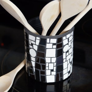 Può includere: Un portautensili in mosaico bianco e nero con cucchiai di legno all'interno. Il portautensili è fatto di piccole piastrelle quadrate e ha un motivo geometrico.