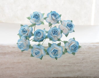 May include: A cluster of light blue paper roses with white centers and green leaves. The roses are arranged in a circular pattern.