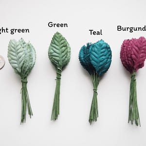 May include: Five bunches of artificial leaves in different colors: light green, green, teal, burgundy. Each bunch is tied together with a thin wire.