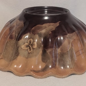 May include: A ceramic bowl with a scalloped edge and a glossy finish. The bowl features a gradient color scheme transitioning from a dark brown at the base to a lighter tan at the rim, decorated with painted brown floral and leaf motifs.