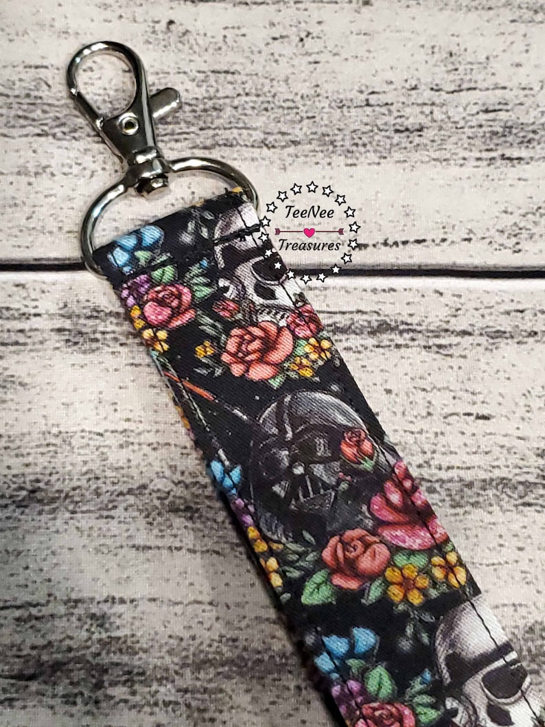 May include: A black and white patterned lanyard with a skull and floral design. The lanyard has a silver clip and a silver ring. The text "TeeNee Treasures" is printed on the lanyard.