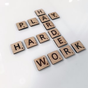 May include: Wooden letter tiles spelling out the phrase "Play Hard Work" on a white surface.