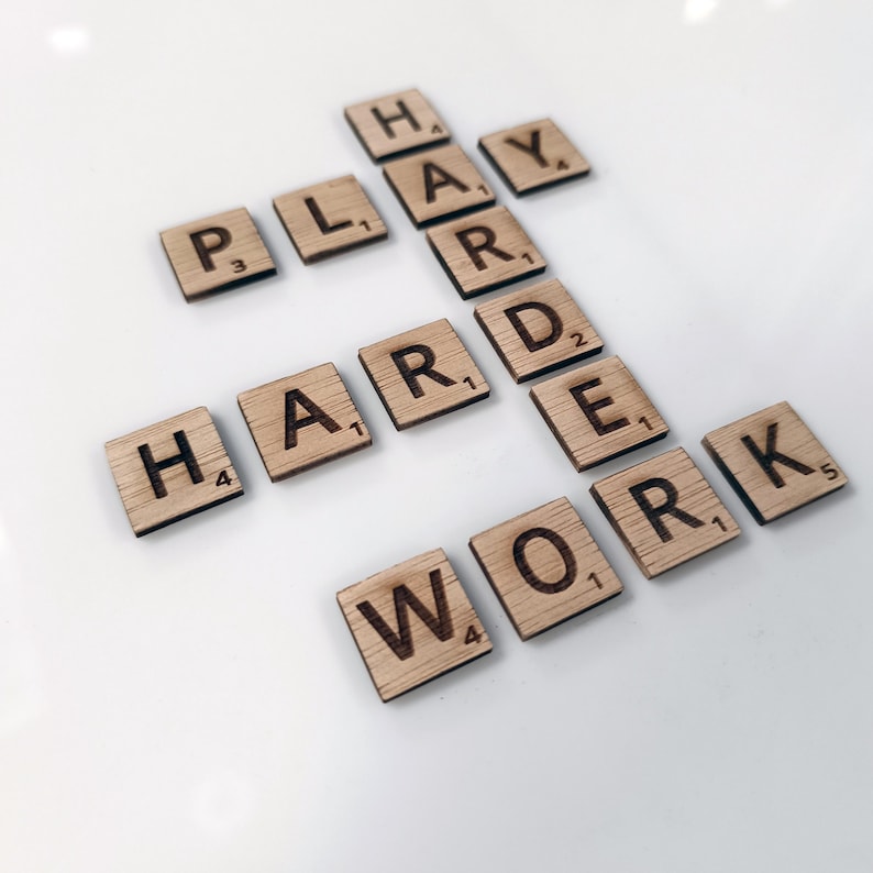 May include: Wooden letter tiles spelling out the phrase "Play Hard Work" on a white surface.