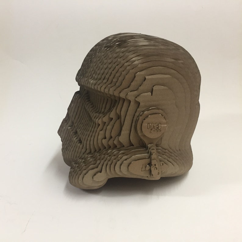 May include: A cardboard model of a helmet, made up of many layers, with a detailed design. The helmet is brown and has a textured surface.