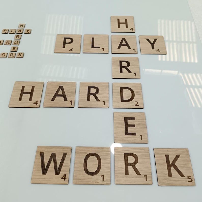 May include: Wooden Scrabble tiles spelling out the phrase "Play Hard Work" on a white background.