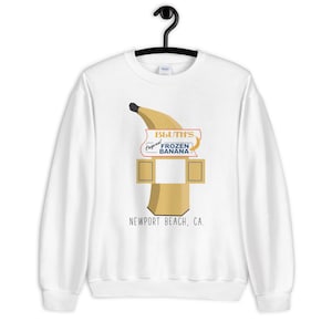 May include: White sweatshirt with a graphic of a banana and a sign that reads "Bluth's Original Frozen Banana - Newport Beach, CA."