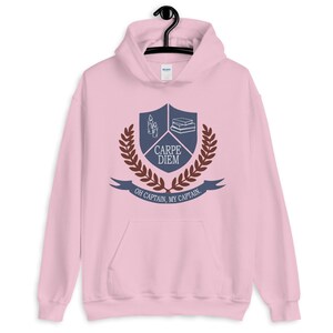 May include: Pink hoodie with a blue and brown crest featuring a book stack, candles, and the text "Carpe Diem" and "Oh Captain, My Captain".
