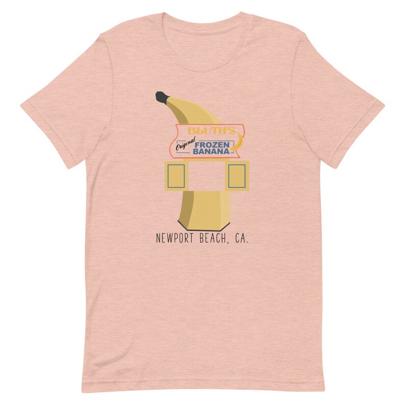 May include: A pink t-shirt featuring a graphic of a yellow banana with a sign that reads "Bluth's Original Frozen Banana" and "Newport Beach, CA."