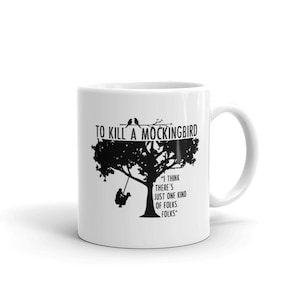 May include: White ceramic mug with a black silhouette of a tree with two birds perched on a branch. The text "To Kill a Mockingbird" is printed above the tree. Below the tree is a quote from the book: "I think there's just one kind of folks. Folks."