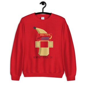 May include: Red sweatshirt with a graphic of a banana and a sign that says "Bluth's Original Frozen Banana, Newport Beach, CA."