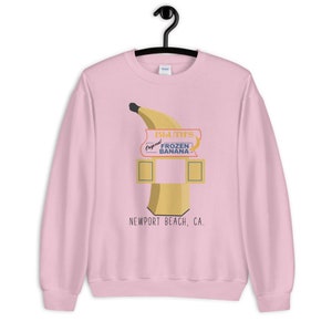 May include: Pink sweatshirt with a graphic of a banana stand with the text "Bluth's Original Frozen Banana" and "Newport Beach, CA."