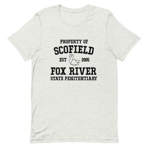 May include: A grey t-shirt with black text that reads "Property of Scofield Est. 2005 Fox River State Penitentiary". A black origami crane is between the words "Est." and "2005".