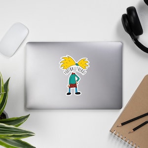 Könnte beinhalten: Ein Aufkleber mit einer Cartoonfigur mit gelben Haaren und dem Text "FOOTBALL HEAD!". Die Figur trägt ein grünes Oberteil und einen rot karierten Rock. Der Aufkleber befindet sich auf einem Laptop.
