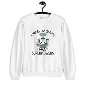 May include: White sweatshirt with the text "FORGET LAB SAFETY! I WANT SUPERPOWERS" and a graphic of lab beakers. The design features a cloud of smoke above the beakers. The sweatshirt is hanging on a black hanger.