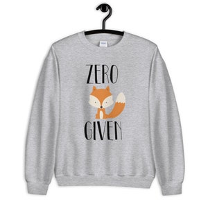May include: A gray sweatshirt with the text "ZERO GIVEN" in black lettering. A cartoon fox with an orange body and white face is sitting below the text.
