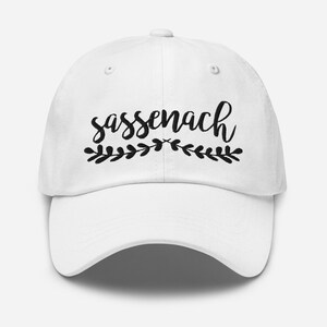 May include: White baseball cap with black embroidery that reads "sassenach" with a small floral design above and below the text.