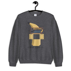 May include: A dark gray sweatshirt with a graphic of a yellow banana and a sign that reads "Bluth's Original Frozen Banana" and "Newport Beach, CA".
