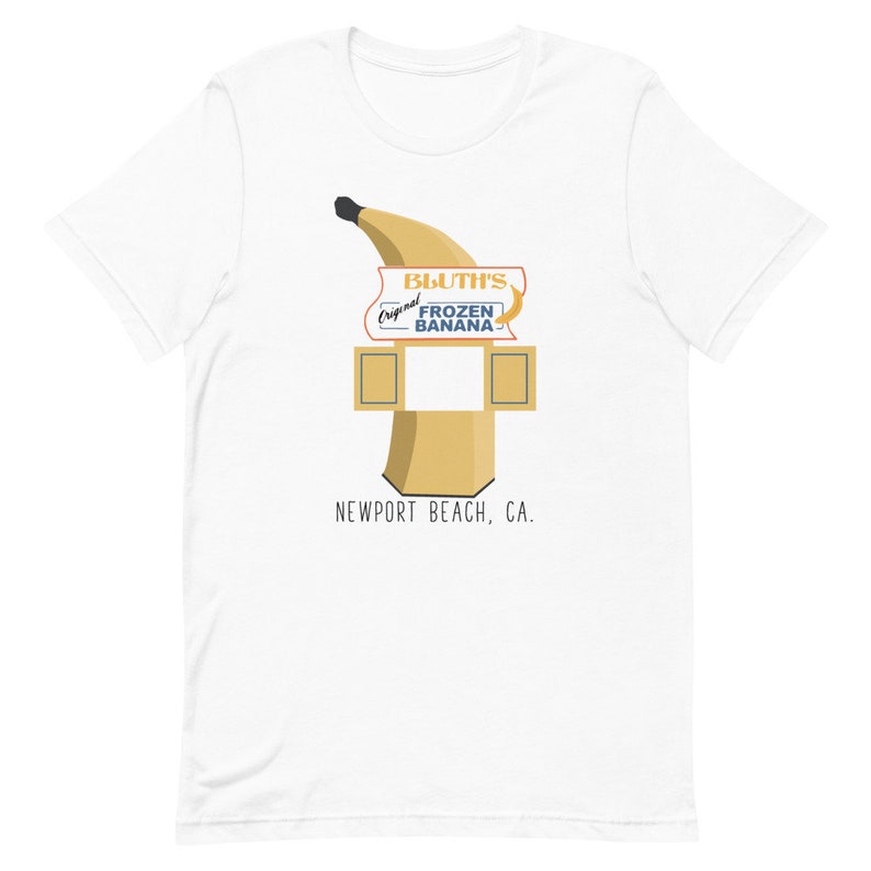 May include: White t-shirt featuring a graphic of a yellow banana and a sign that reads "Bluth's Original Frozen Banana" and "Newport Beach, CA."