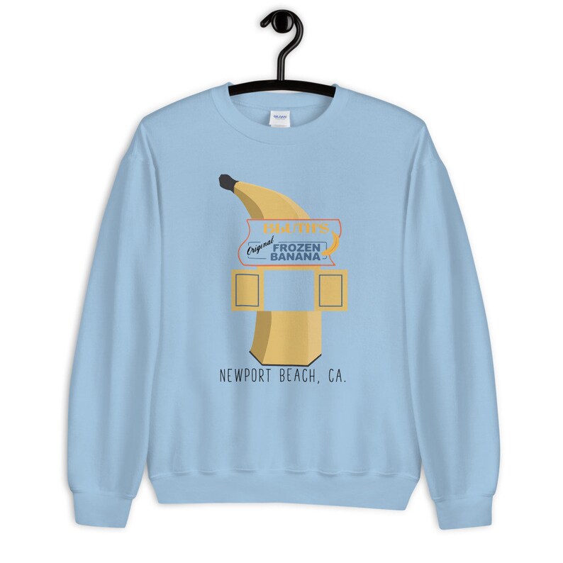 May include: Light blue sweatshirt with a graphic of a banana-shaped frozen banana stand with the text "Doug's Original Frozen Banana" and "Newport Beach, CA."