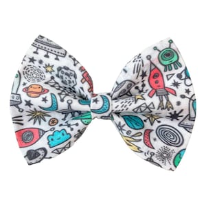 May include: A white bow tie with a colourful space-themed print featuring rockets, planets, stars, and aliens.