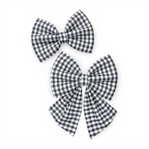 May include: Two black and white gingham fabric bows. The bows are in a classic bow shape, with a symmetrical design. The fabric has a checkered pattern. The bows are set against a white background.