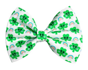 May include: A white bow tie with a green shamrock pattern and rainbows. The shamrocks have smiling faces.