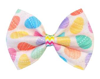 May include: A white bow with a pastel Easter egg pattern. The bow has a yellow, green, and white zig-zag pattern in the center.