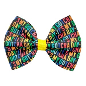 May include: A black bow with a yellow centre, featuring a rainbow print of the text "It's My Gotcha Day".