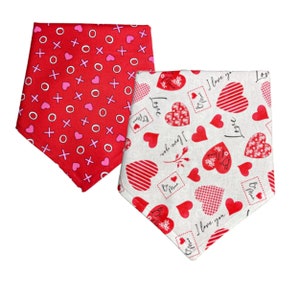 May include: Two red and white patterned dog bandanas. One bandana has pink hearts and red x's and o's. The other bandana has a white background with red hearts and the text "I love you" repeated.